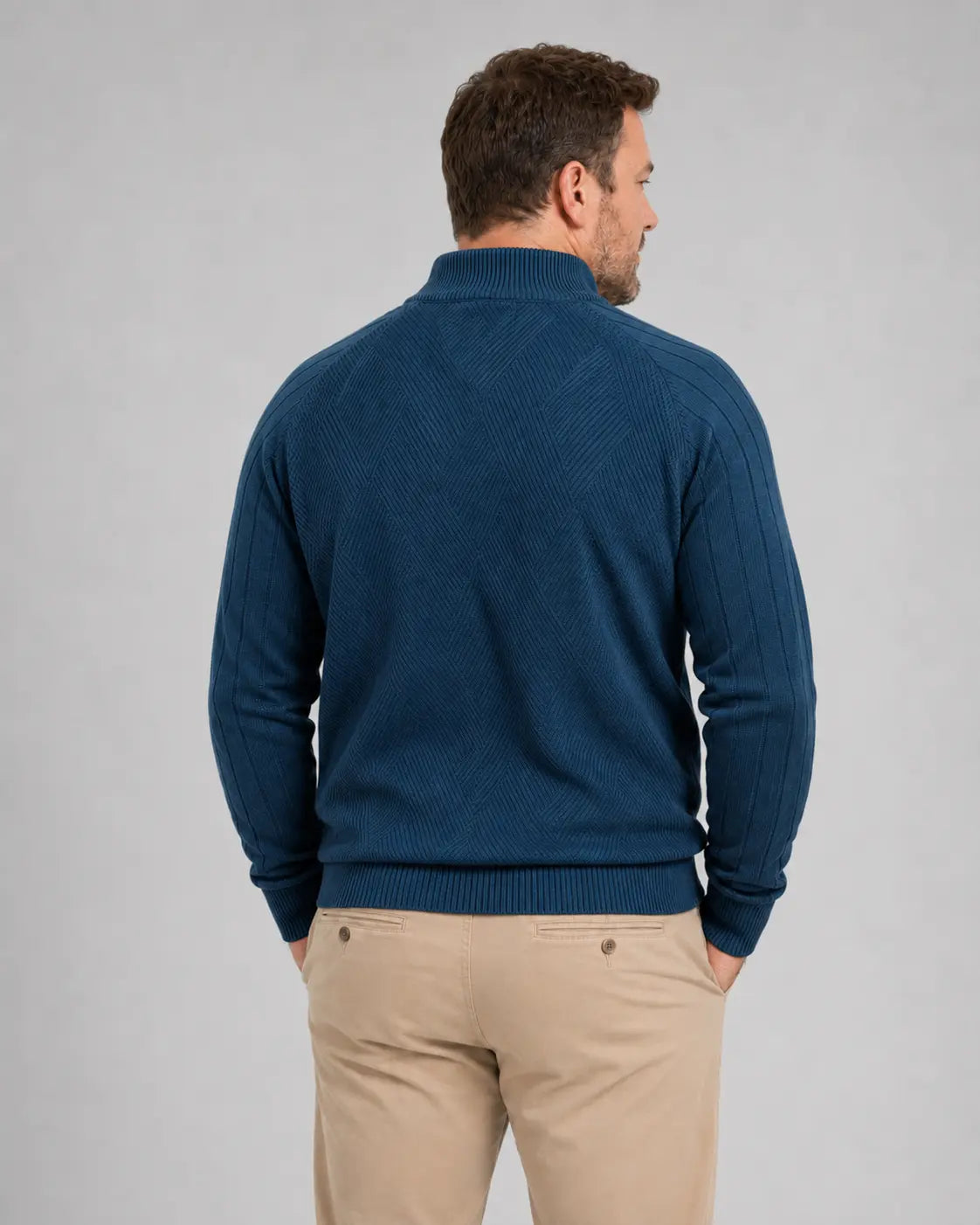Homem de costas usando suéter azul-marinho com gola alta, mangas longas e barra canelada. A parte traseira apresenta uma trama geométrica em losangos e caimento confortável sobre a calça bege.