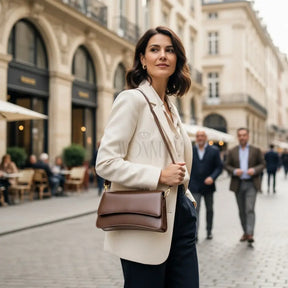 Modelo feminina AVONNUE com blazer claro e bolsa marrom estruturada, em cenário urbano sofisticado e atemporal.