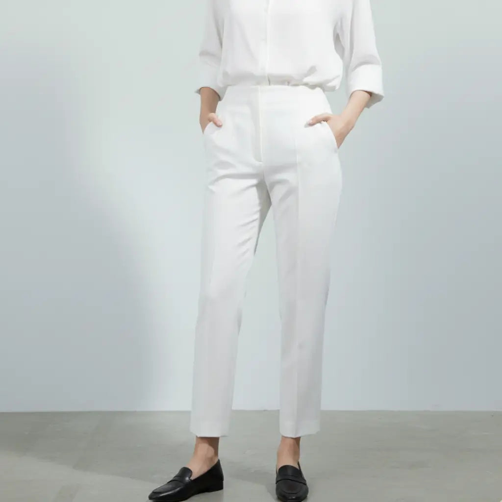 Mulher vestindo calça social branca feminina com camisa branca e sapato preto, modelagem reta e cintura alta.