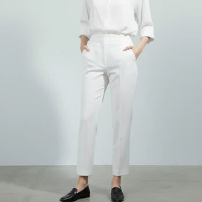 Mulher vestindo calça social branca feminina com camisa branca e sapato preto, modelagem reta e cintura alta.