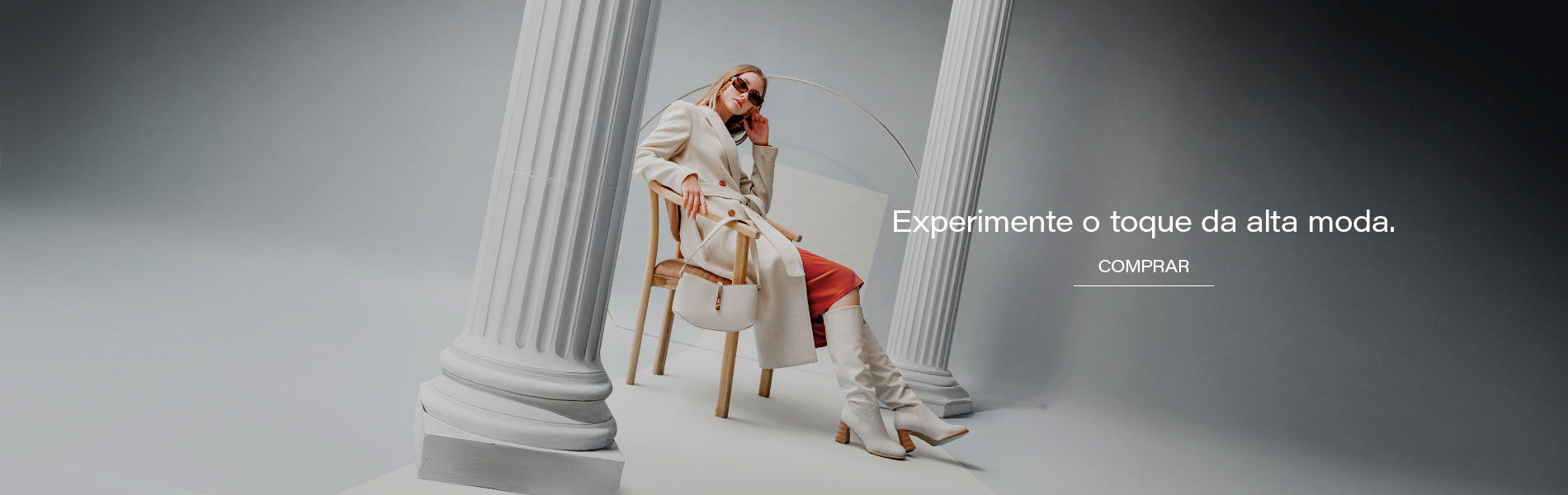 Banner editorial AVONNUE com modelo feminina em sobretudo claro estruturado, bolsa sofisticada e cenário arquitetônico minimalista.