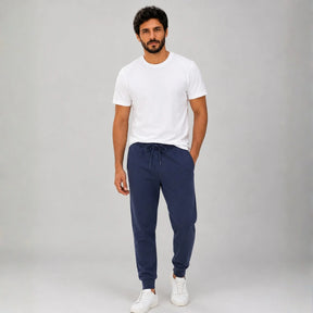Homem vestindo calça de moletom masculina azul marinho de frente com camiseta branca e tênis branco