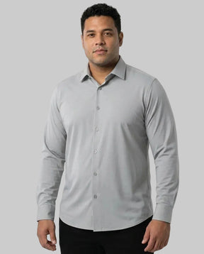 Homem de frente vestindo a Camisa Social Tech Vitto cinza-claro, de mangas longas e botões no mesmo tom, combinada com calça preta em fundo branco.